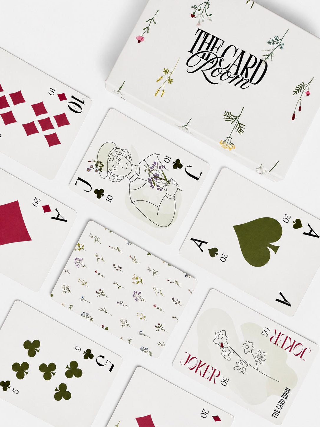 A styled flat-lay of a deck of illustrated playing cards on a white background, showing several cards including the Joker, Jack of Hearts, Ace of Clubs, and a 10 of Diamonds, with floral and minimalist artwork.