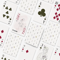 A flat-lay arrangement of playing cards on a white background, featuring a white card with a delicate pink floral design and the text 'THE CARD ROOM' alongside 'JOKER'.